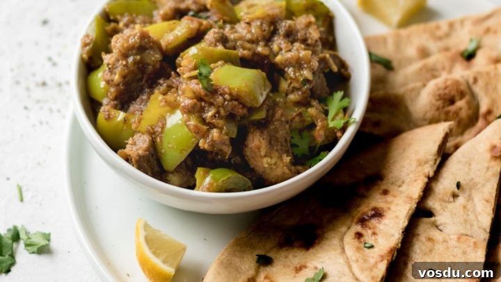 Bowl of Instant Pot Goat and Bell Pepper Curry garnished with cilantro on top of a white plate with naan and lemon wedges.