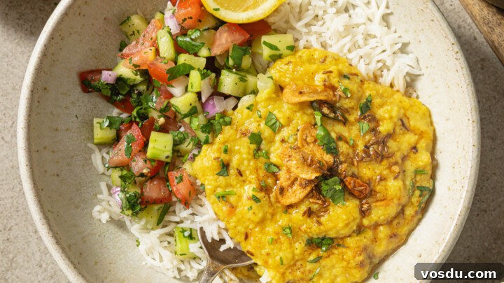 A bowl of basmati rice topped with Moong Dal with Kachumber salad on the side with a squeezed lemon wedge.