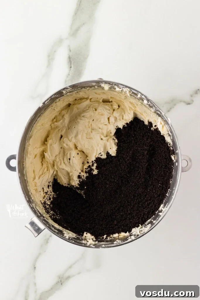 vanilla buttercream frosting in a large silver bowl with crushed gluten free Oreo crumbs to make a Cookies and Cream Frosting Recipe