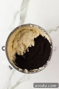 vanilla buttercream frosting in a large silver bowl with crushed gluten free Oreo crumbs to make a Cookies and Cream Frosting Recipe