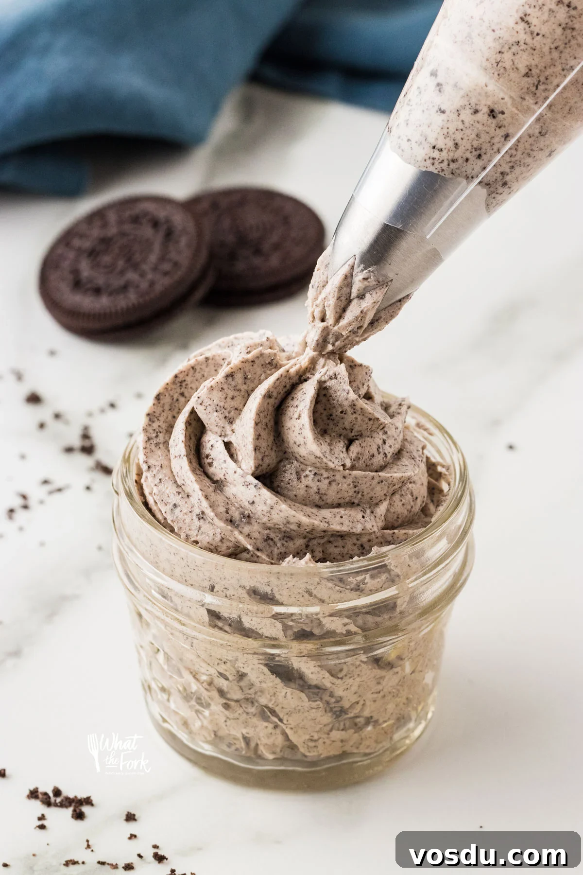 Cookies and Cream Frosting Recipe being piped into a small glass jar with a piping bag fitted with a large open star tip
