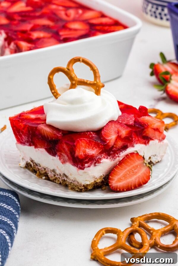 Layers of strawberry jello, pretzel crust and cream cheese filling, on a black plate.