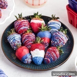 Red, white, and blue, dipped strawberries, placed side by side on a dark blue plate.