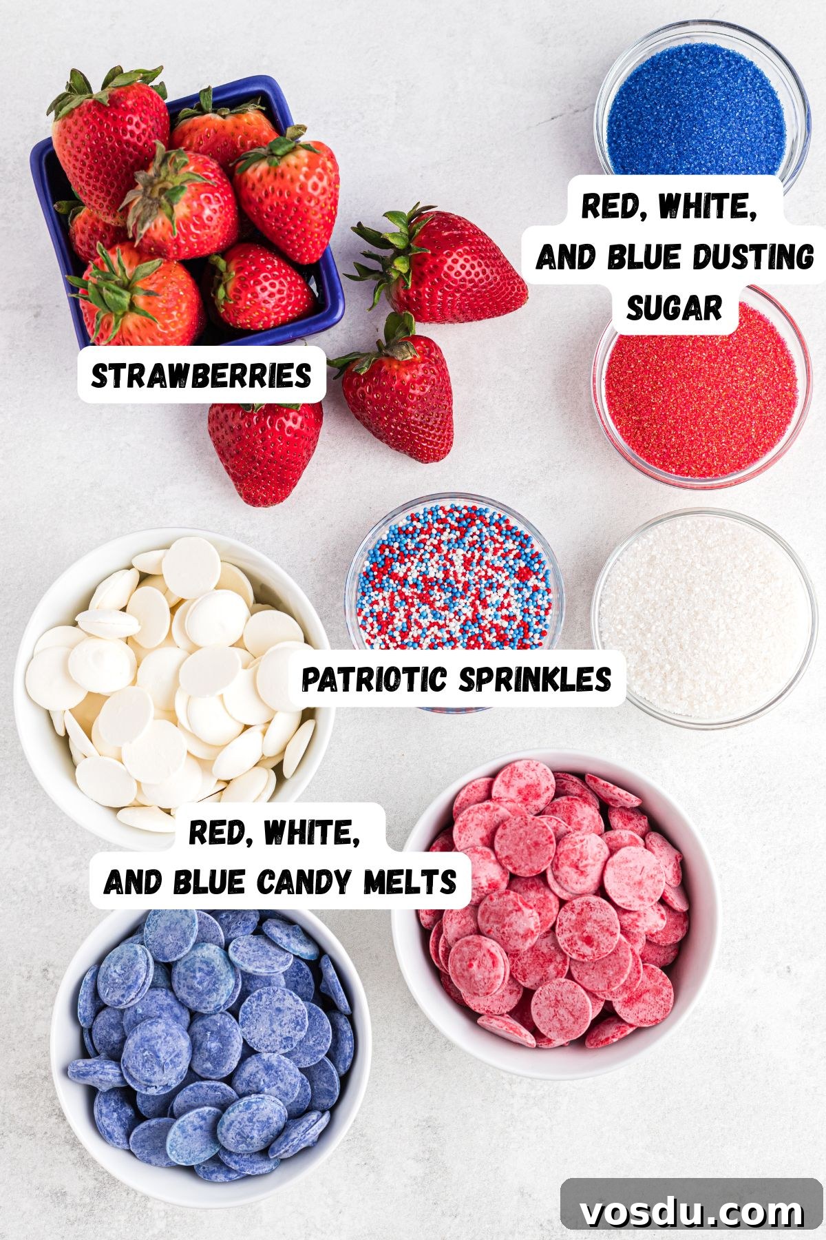 Strawberries, dusting sugar, sprinkles, and candy melts measured into small dishes on a white marble table.