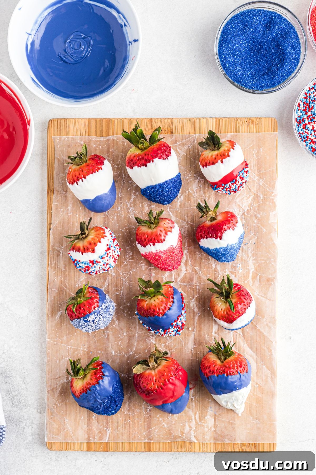 Dipped and decorated strawberries resting to dry on a small wooden cutting board.