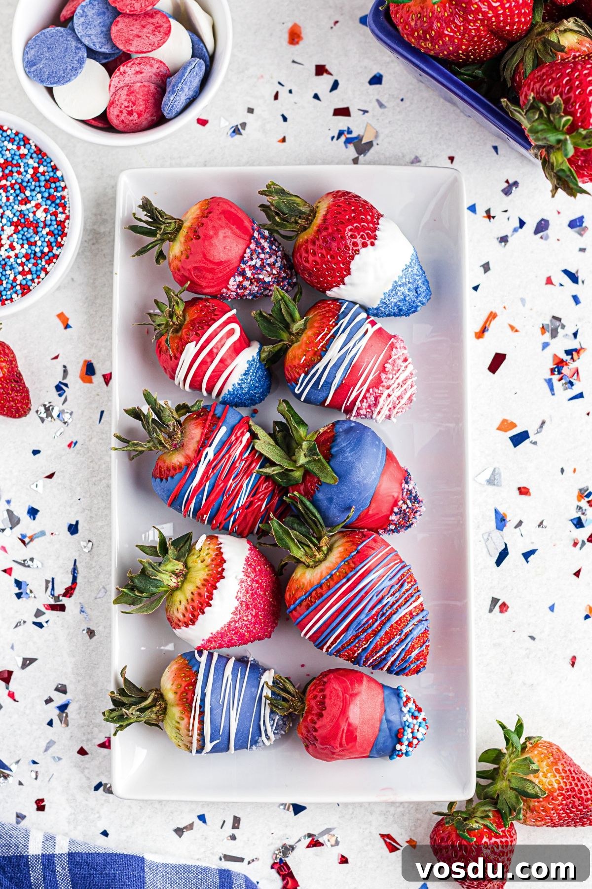 Patriotic berries on a rectangle plate with sprinkles and extra strawberries scattered around the plate.