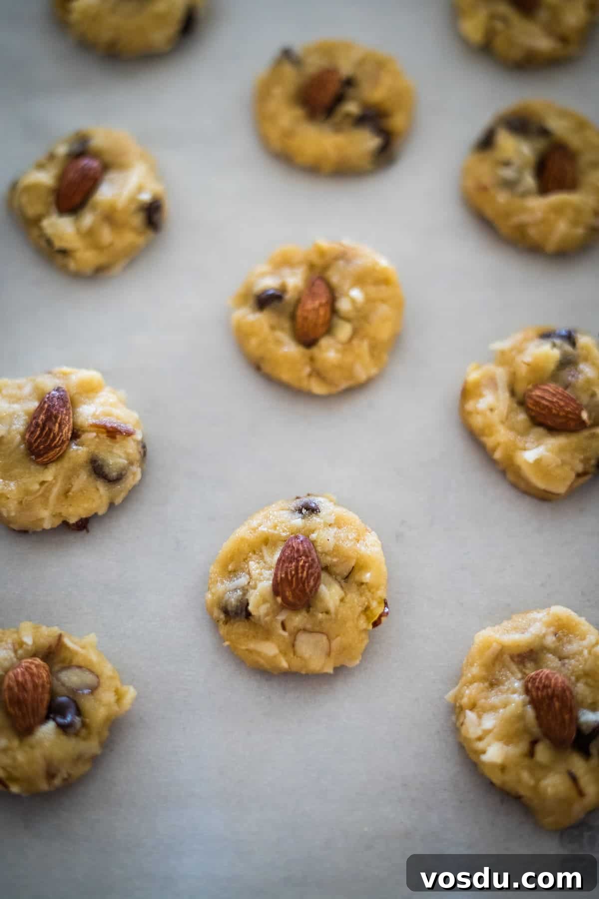 Keto Almond Joy Cookies Recipe — Low-Carb Coconut Chocolate Cookies 9 Unbaked cookie dough balls with almonds on a baking sheet.