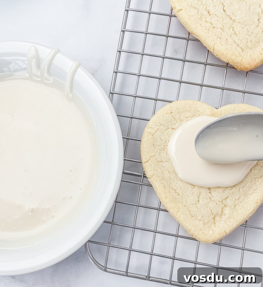Almond Flour Shortbread Cookies Recipe — Buttery Gluten-Free Treat 8 Icing a heart shaped cookie on a wire rack with white icing using a spoon. A bowl of icing is next to the cookie.