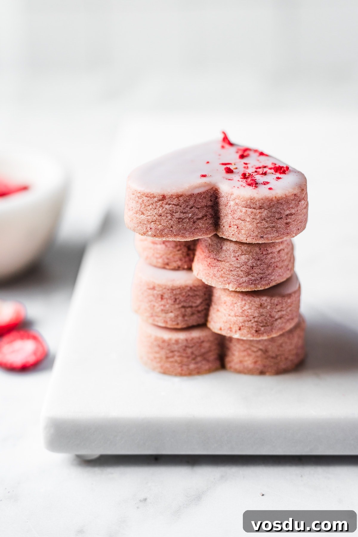Strawberry Shortbread Cookies Recipe — Simple Homemade Treat 3 A stack of four glazed pink heart shaped cookies on a marble tray.