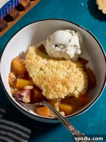 Sourdough Peach Cobbler in a bowl with a scoop of vanilla ice cream.