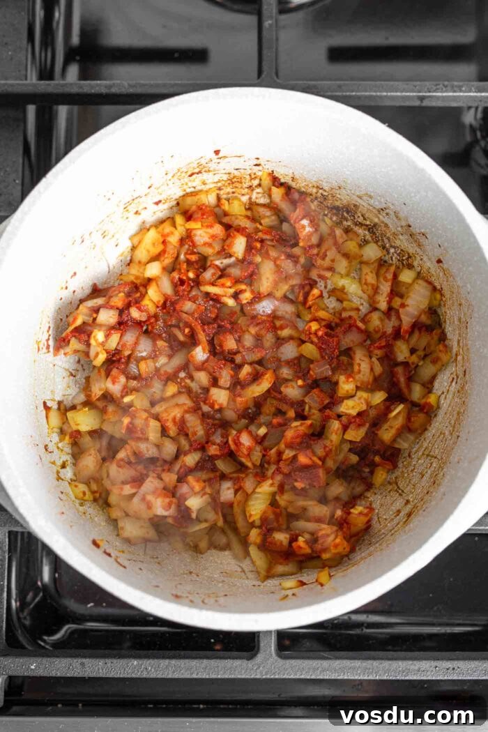 Hearty Sweet Potato and Red Lentil Stew Recipe 4 Onion, garlic, ginger and tomato paste cooking in a large soup pot on a gas range.