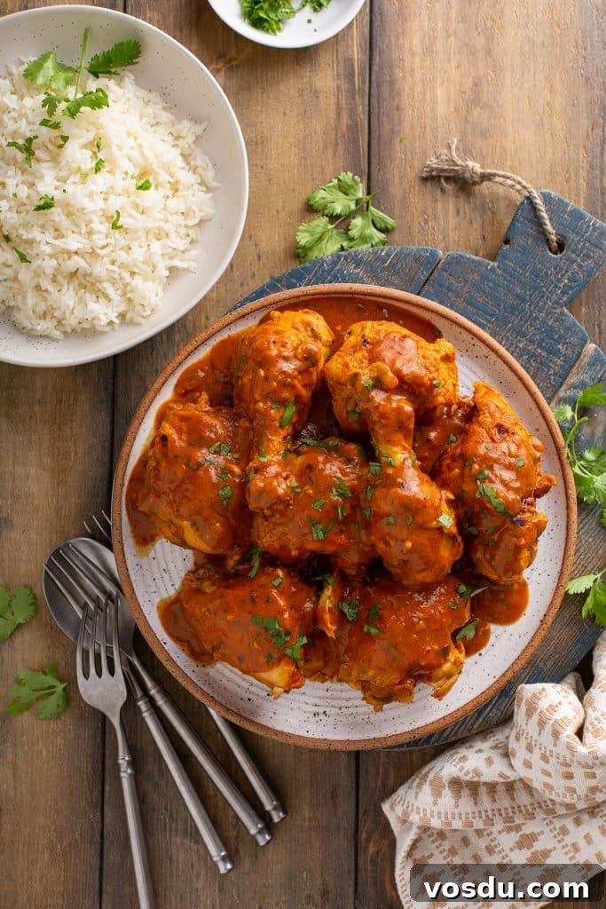 Chicken masala on a plate next to a bowl with rice.