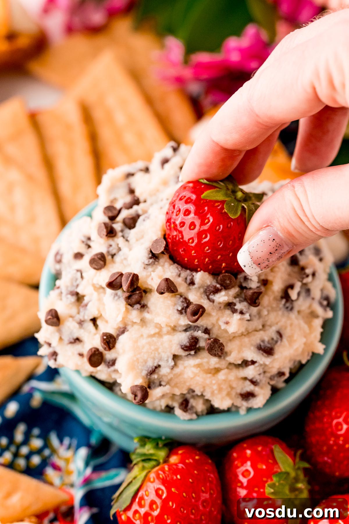 Mascarpone Cannoli Dip Recipe: Creamy Dessert Dip for Parties 6 A woman's hand dipping a strawberry in a dessert dip with mini chocolate chips.