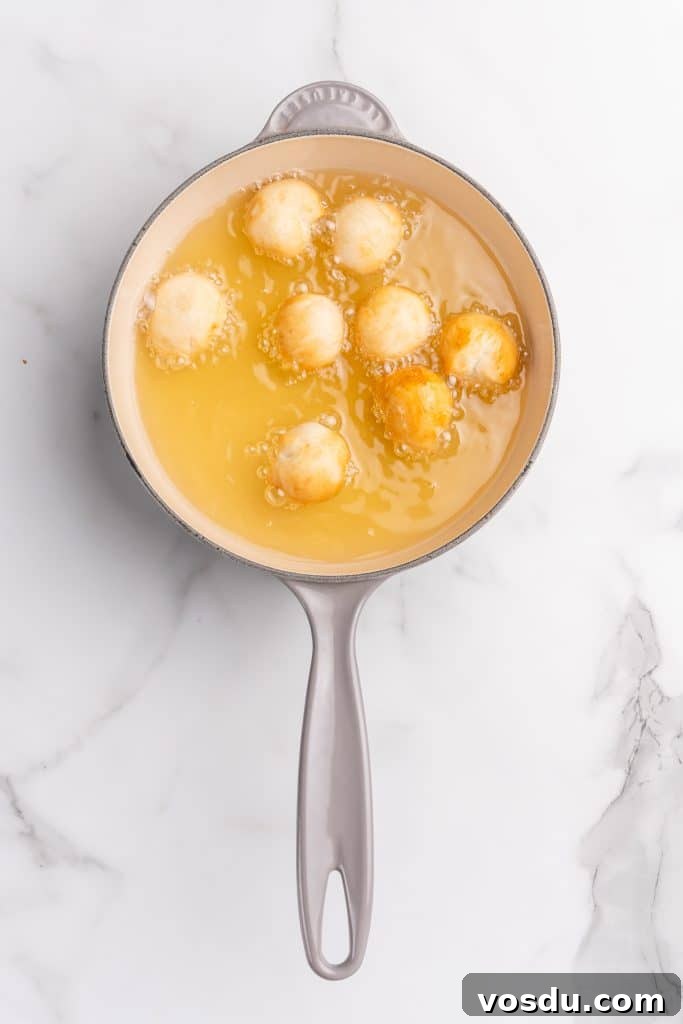 balls of biscuit dough frying in oil in a gray skillet
