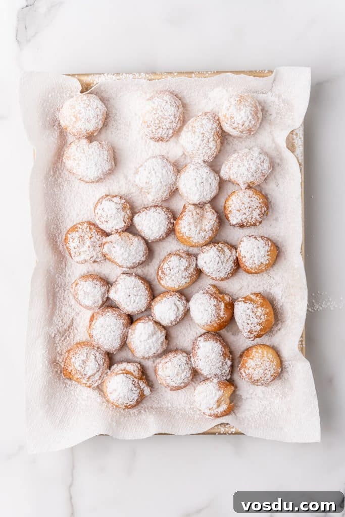 powdered sugar coated beignets on a paper towel lined baking pan