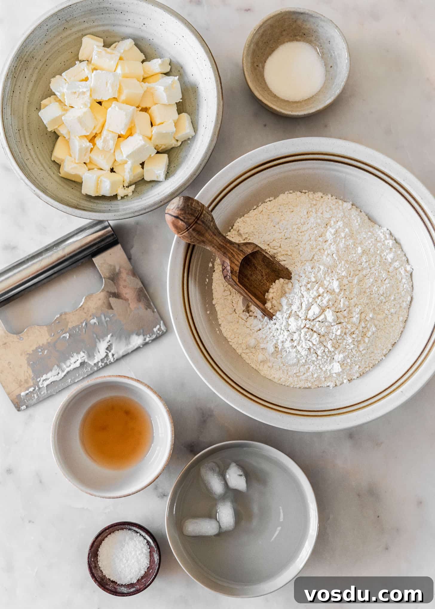 The Ultimate Pie Crust Recipe That Will Wow Your Guests 3 Ingredients for homemade pie dough in white and grey bowls on a white marble counter.