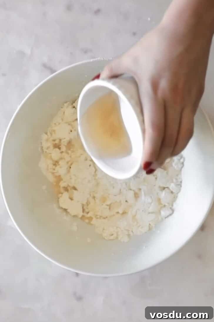 The Ultimate Pie Crust Recipe That Will Wow Your Guests 5 A hand pouring cold water into a white bowl of flour and butter.