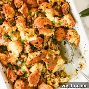 Savory Sausage Stuffing Recipe for Holiday Dinners 11 A baking dish full of sausage stuffing with a portion missing and a serving spoon sticking out.