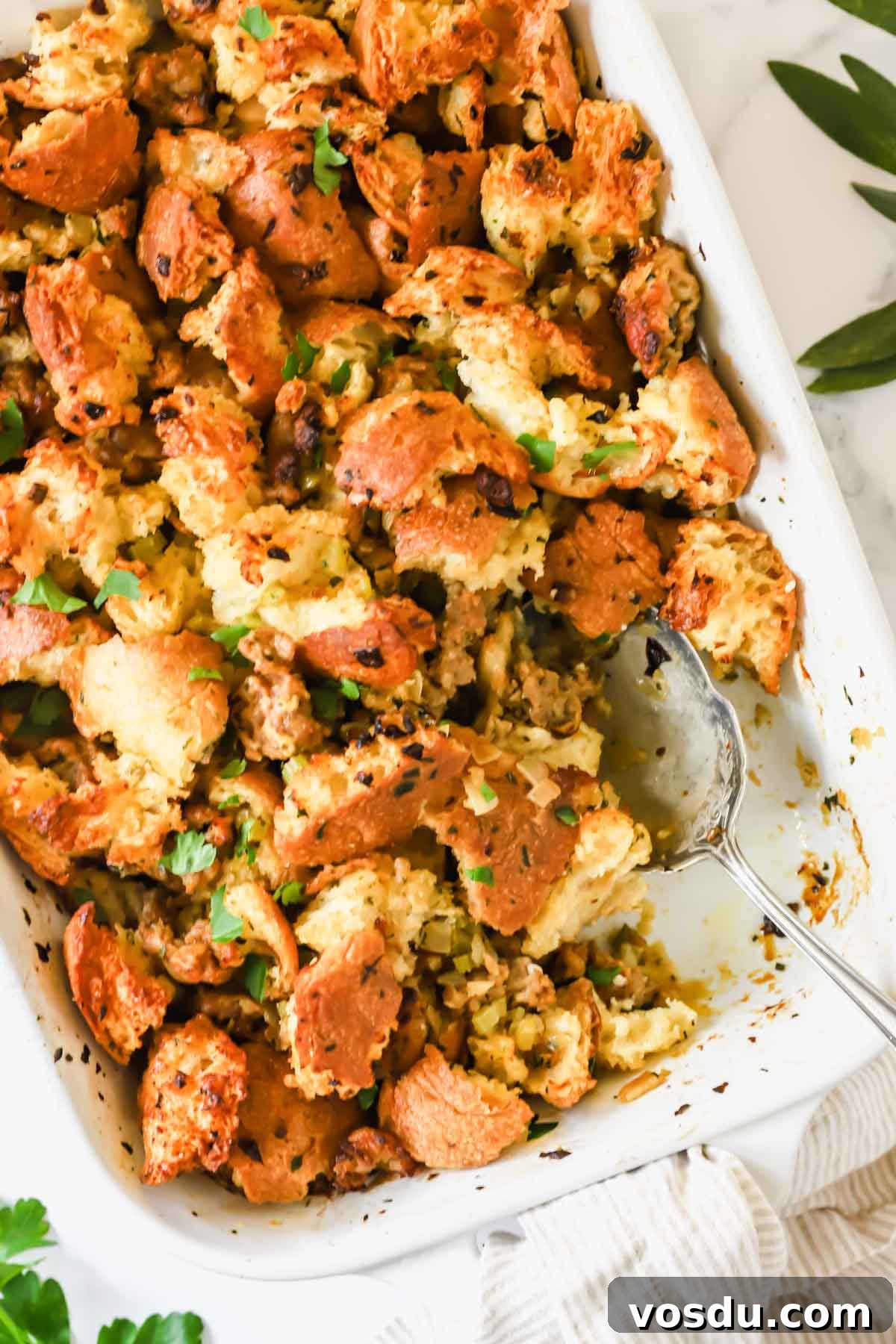 Savory Sausage Stuffing Recipe for Holiday Dinners 3 A baking dish full of sausage stuffing with a portion missing and a serving spoon sticking out.