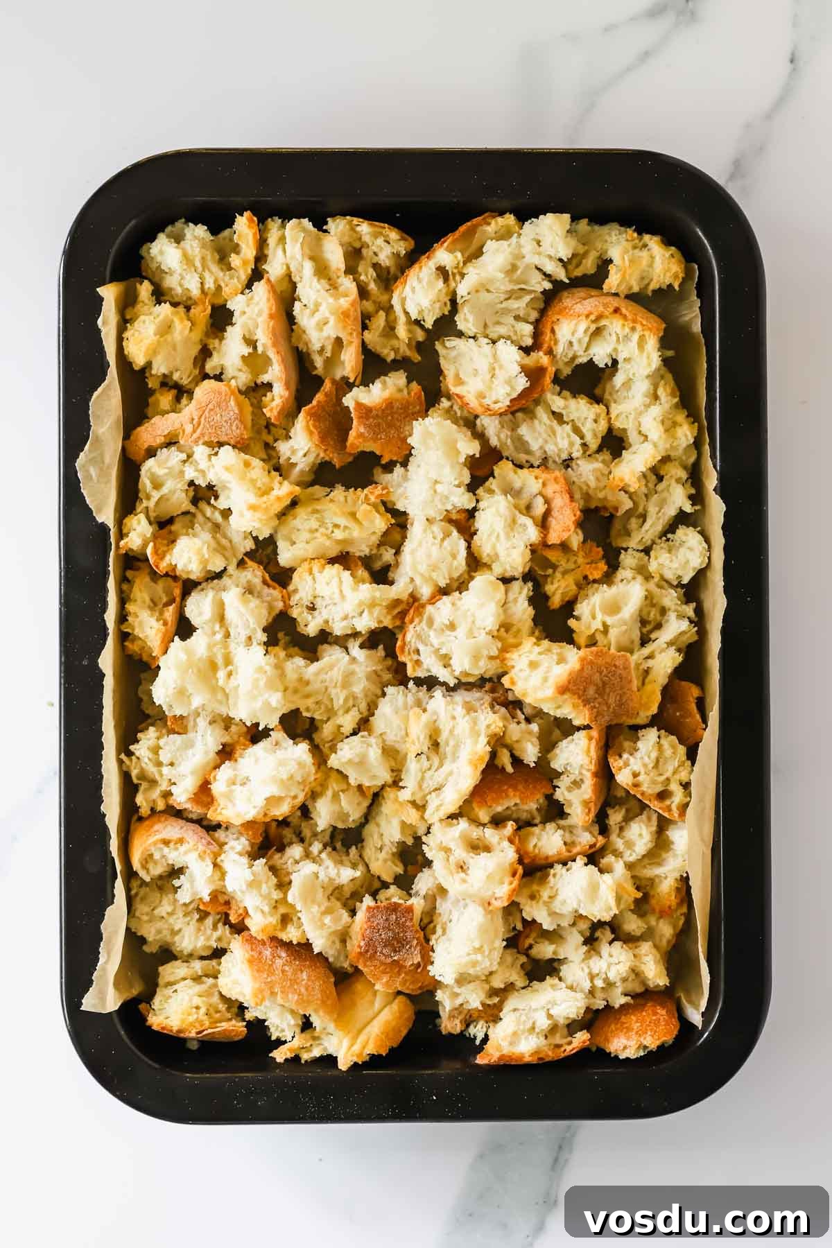 Savory Sausage Stuffing Recipe for Holiday Dinners 5 Bread cubes in a rimmed baking sheet lined with parchment paper.
