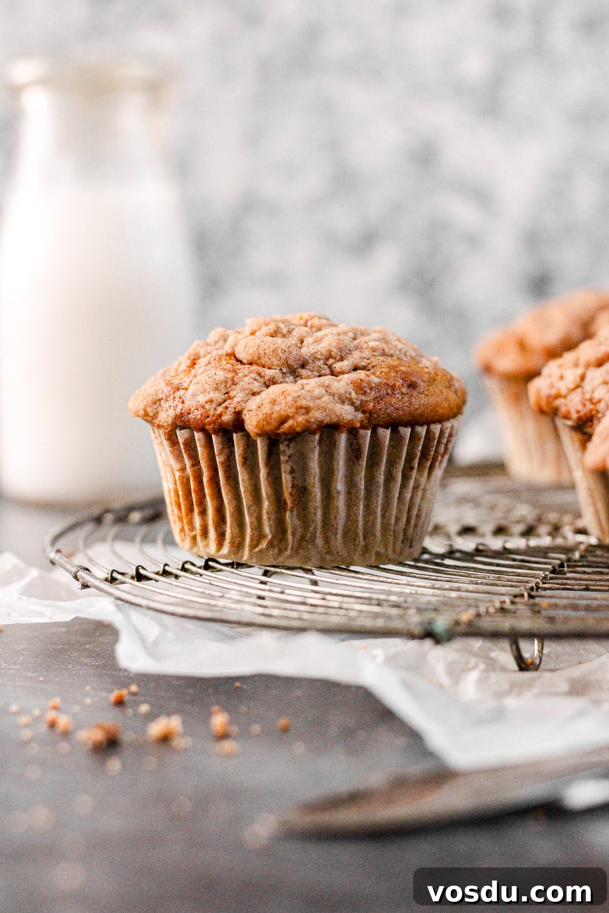 cinnamon banana muffin with streusel topping on a cooling rack with a milk jug for baking blog