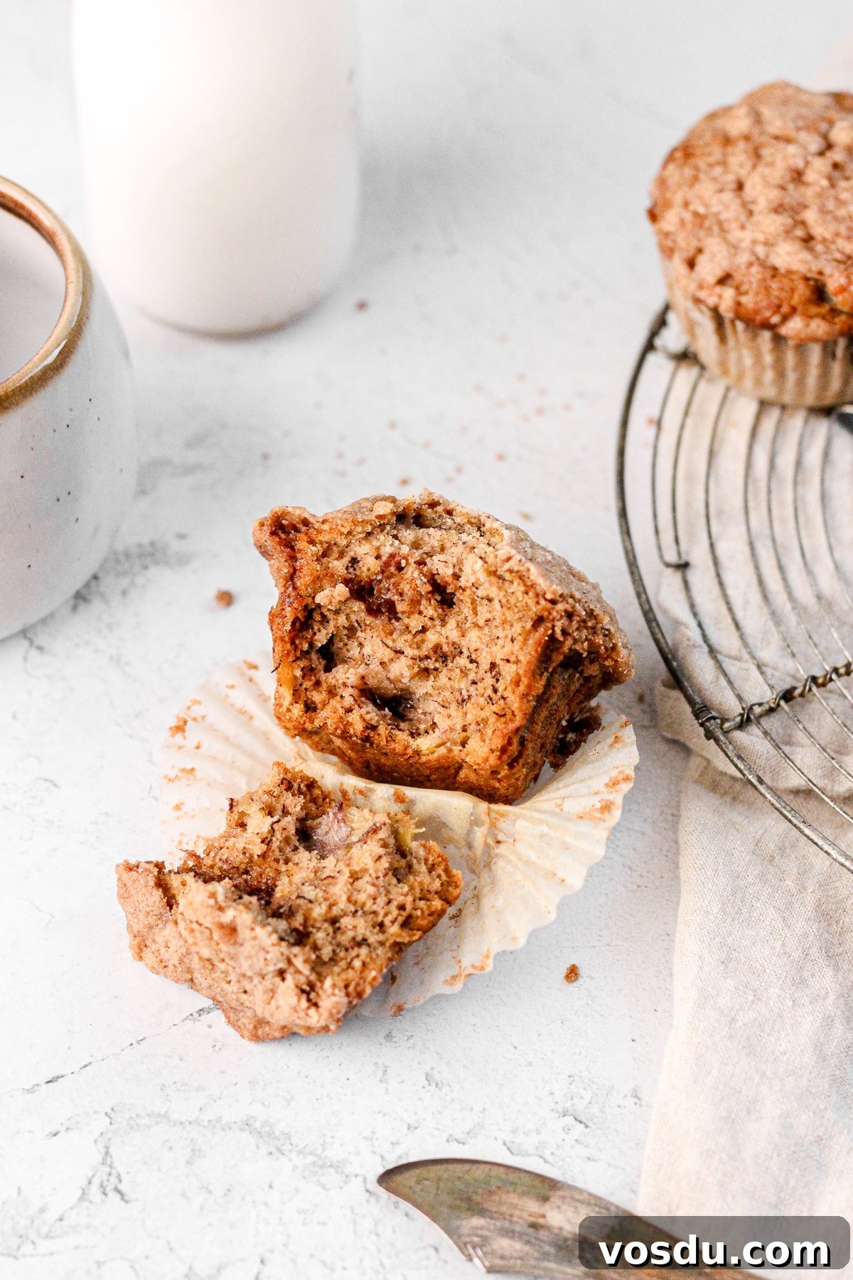 a banana muffin cut in half with a milk jug and wire cooling rack for food photography