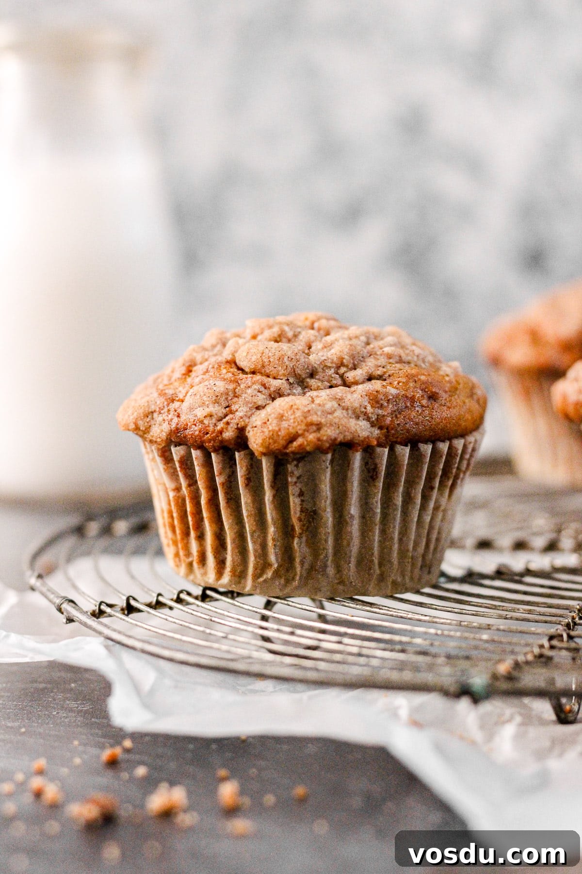 cinnamon banana muffin with streusel topping on a wire cooling rack with a milk jug for baking blog