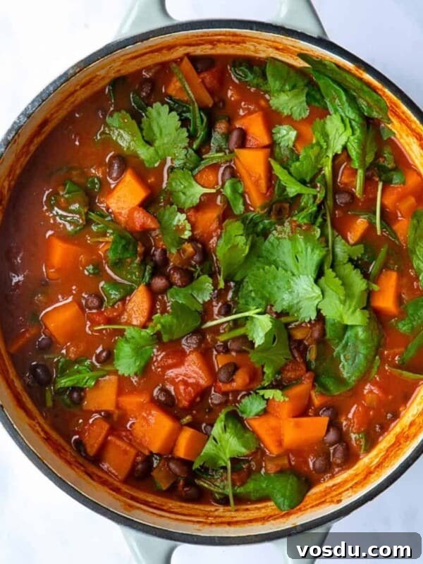 15-Minute Chickpea Stew Recipe for Quick Weeknight Dinners 7 Sweet Potato and Black Bean Stew served in a large pot topped with coriander. The pot is displayed on a white marble background.
