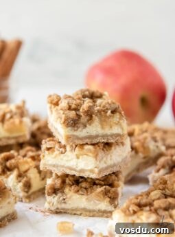 stack of three apple cheesecake bars showing layers of shortbread crust, cheesecake, apples and streusel