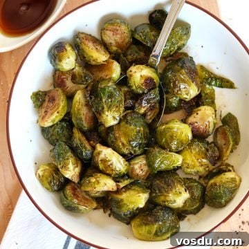 Maple-Balsamic Glazed Brussels Sprouts — Air Fryer or Oven 5 Maple balsamic roasted brussels sprouts in a a round white bowl with a brown rim and a serving spoon.