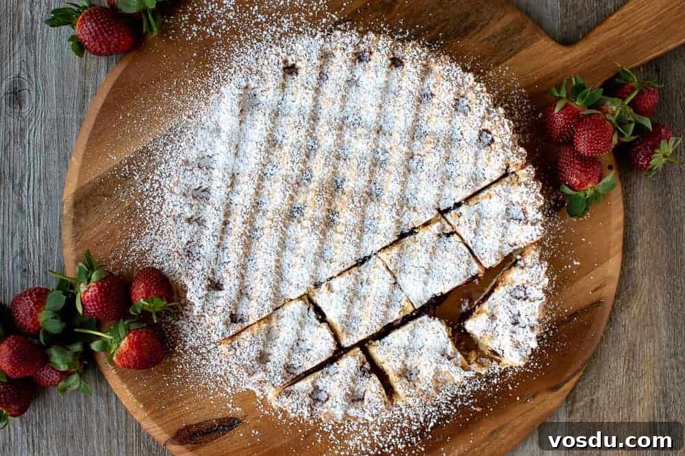 This Strawberry Crostata recipe | Easy Strawberry Tart is an easy Italian pastry filled with fruity jam #strawberrycrostata #crostatarecipe #strawberrytart #crostatadough Strawberry crostata recipe dusted with powdered sugar with a few squares cut.