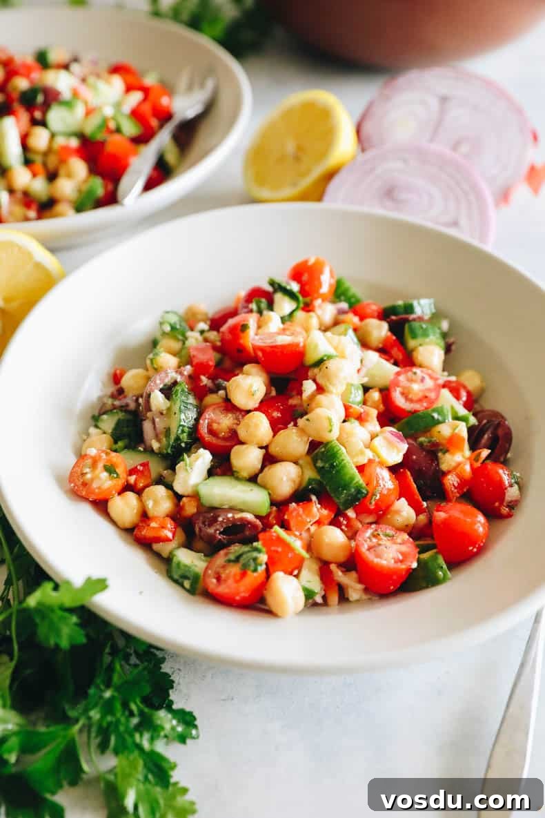 Mediterranean Chickpea Salad with Lemon-Herb Vinaigrette 2 chickpea salad with tomatoes, cucumbers, olives and feta in a white bowl.