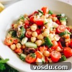Mediterranean chickpea salad recipe in a white shallow bowl with tomatoes, cucumbers, peppers, parsley and feta.