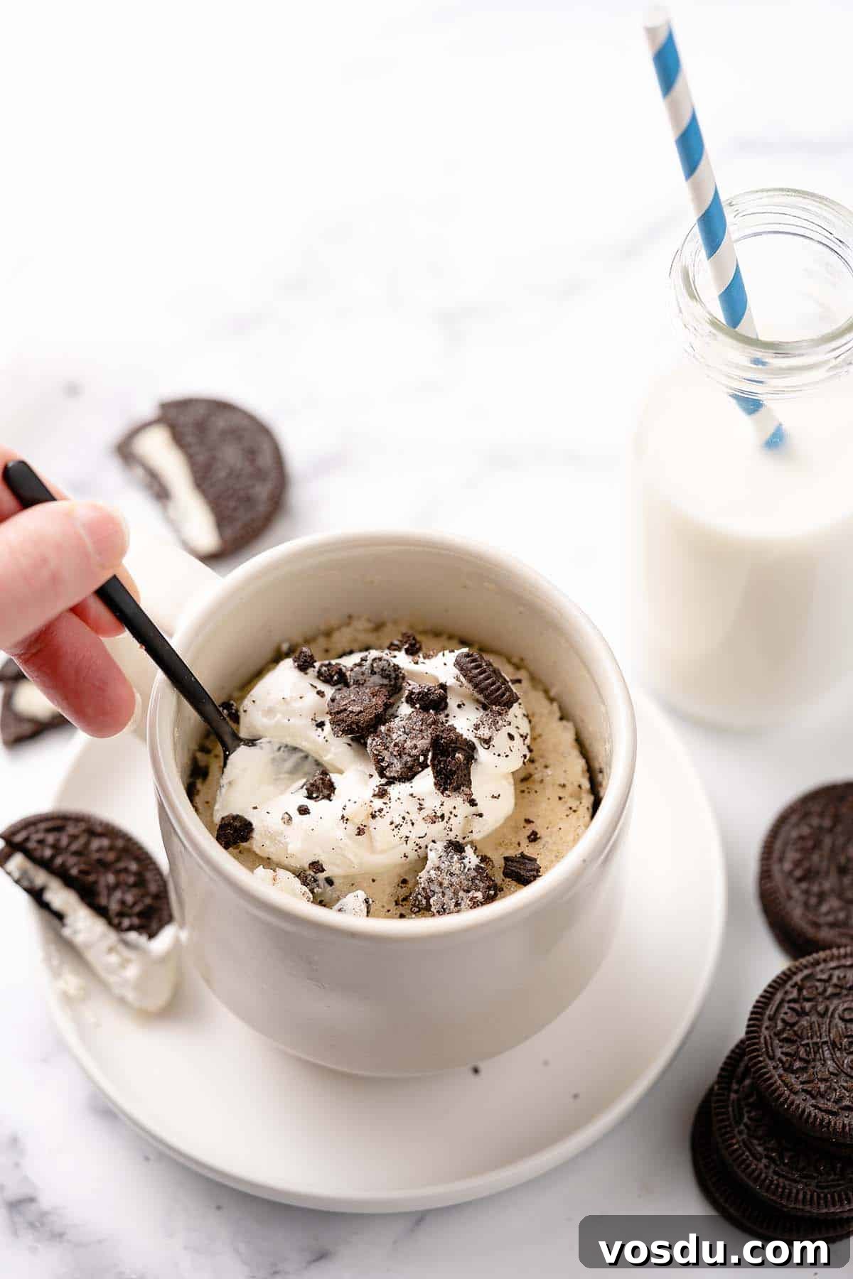 3-Minute Oreo Mug Cake Recipe You Can Make in a Microwave 2 Mug cake with whipped cream and Oreos on top with spoon scooping out a bite