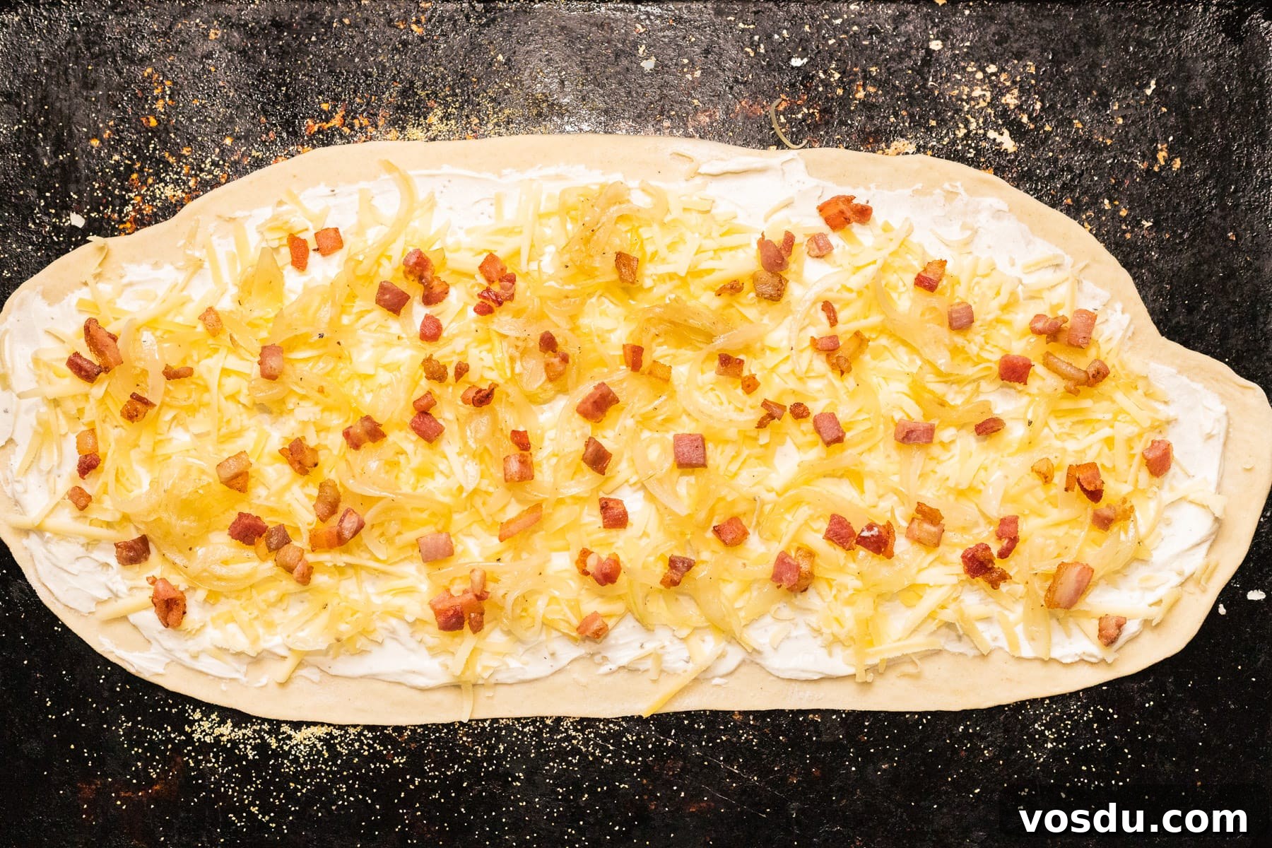 A top down view of unbaked flammkuchen on a baking sheet.