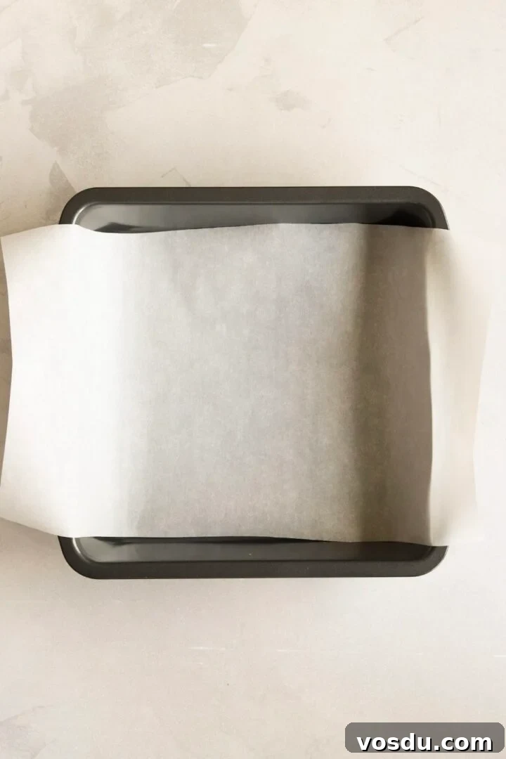 8x8-inch baking pan lined with parchment paper, sitting on a white marble counter
