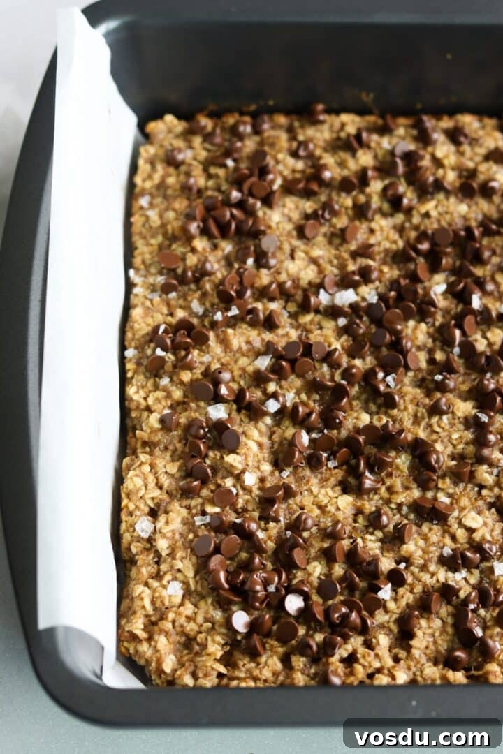 Fresh-baked banana peanut butter oat bars topped with mini chocolate chips and flakey sea salt, in a parchment-lined baking pan