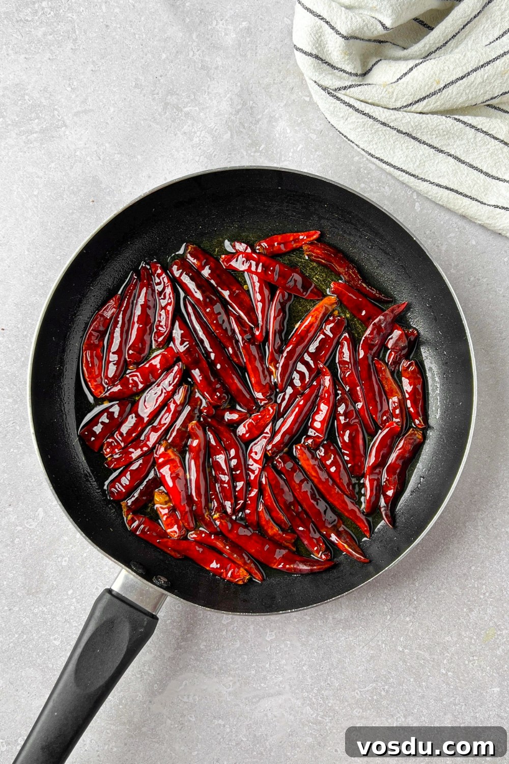 Dried peppers being fried in oil in a pan.