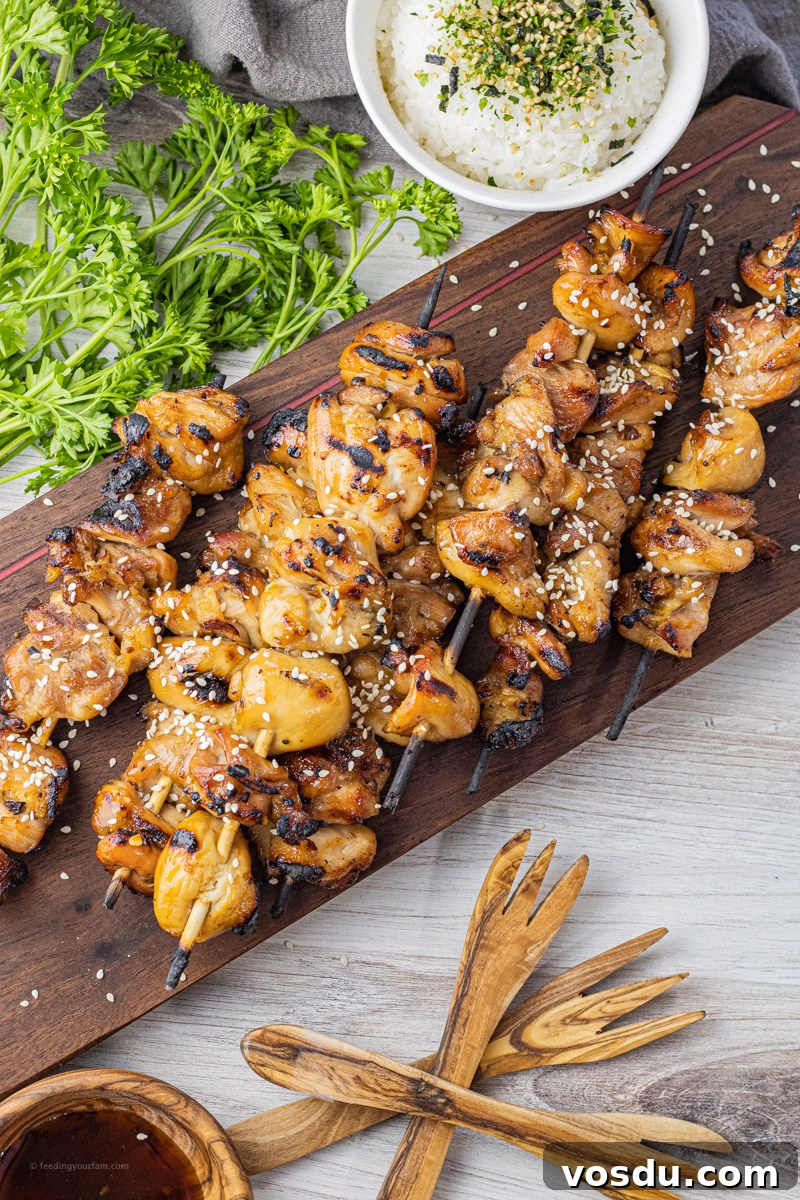 Sticky Teriyaki Chicken Skewers with Sesame and Green Onion 2 chicken kabobs that have been grilled and topped with sesame seeds on a dark wooden board
