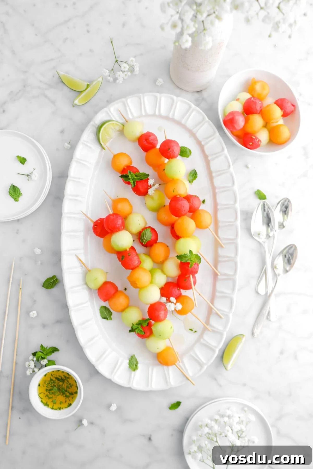 melon skewers on white platter with mint sprigs and white flowers