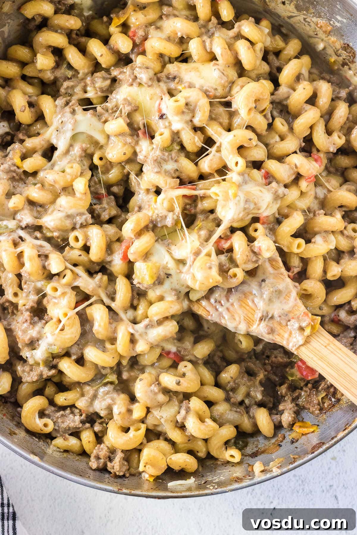 One-Pot Philly Cheesesteak Pasta Recipe for Fast Weeknight Dinner 6 Overhead view of a pan of pasta with a wooden spoon in it showing the gooey, cheesy top.