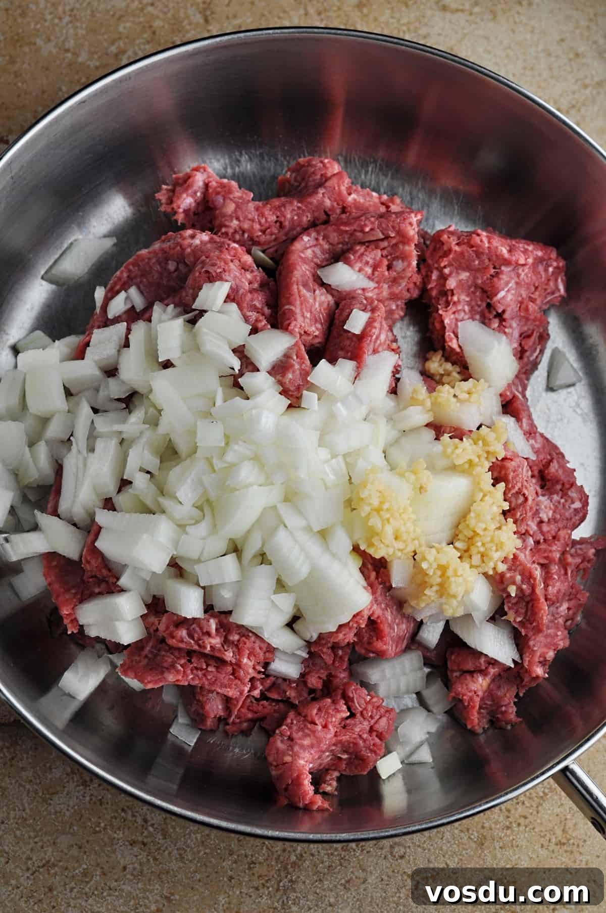 Slow Cooker Hungarian Goulash Recipe for Tender Beef 4 Uncooked ground beef, chopped onion, and minced garlic in skillet ready to cook.