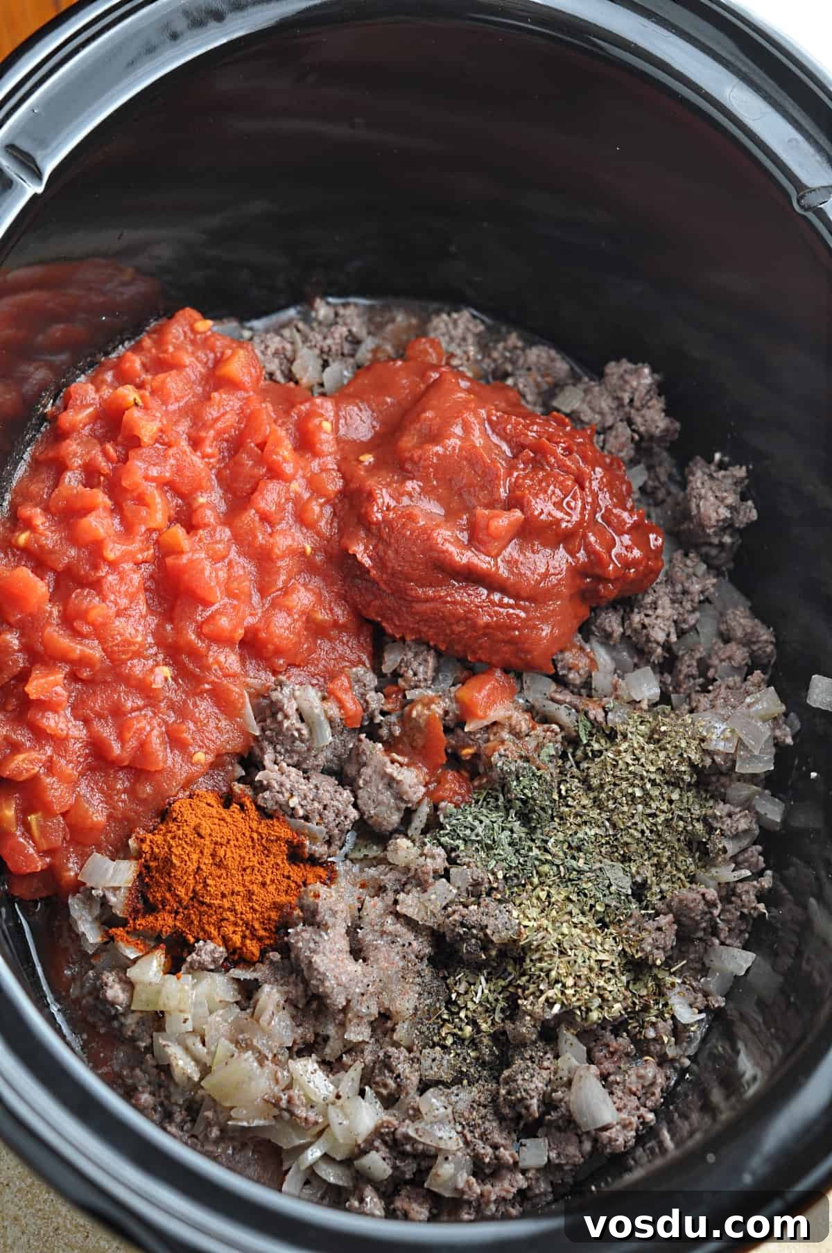 Slow Cooker Hungarian Goulash Recipe for Tender Beef 6 Tomatoes and seasonings on top of cooked ground beef and onions in slow cooker.