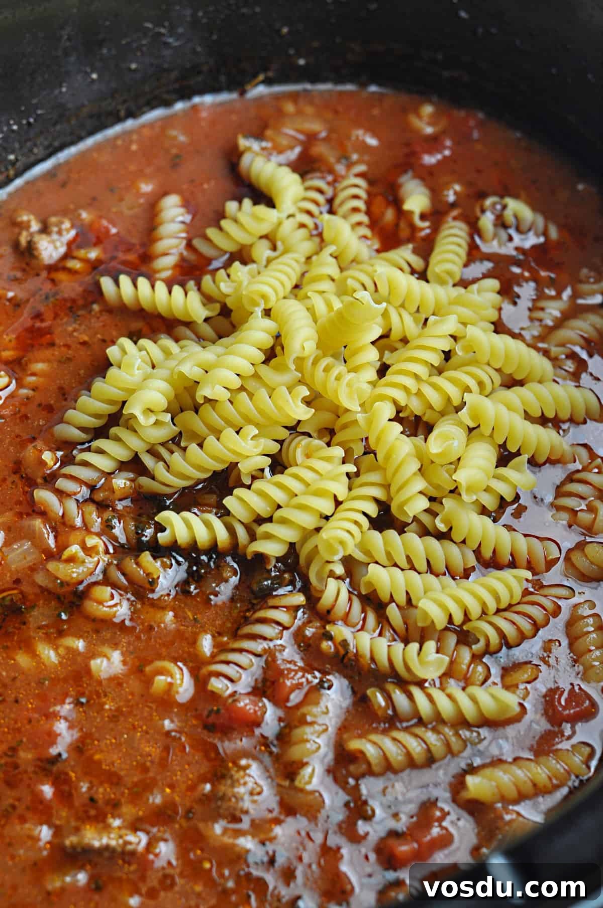 Slow Cooker Hungarian Goulash Recipe for Tender Beef 7 Uncooked pasta on top of ground beef and tomato mixture in slow cooker.