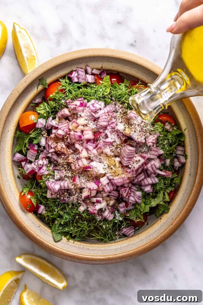 pouring olive oil into fresh tomato relish with herbs and lemon for Greek beef bowls