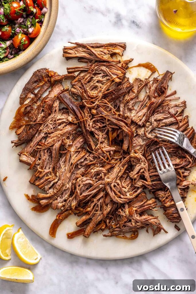 Tender slow-cooked Greek beef being shredded with forks
