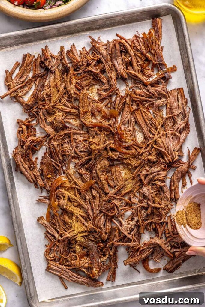 adding the remaining spice blend to the shredded flank steak on a sheet pan