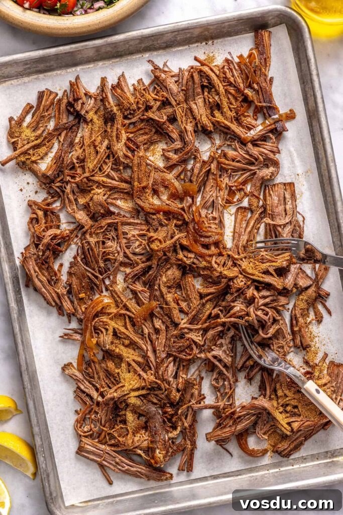 Shredded flank steak on a sheet pan after cooking in a crock-pot for Greek beef bowls