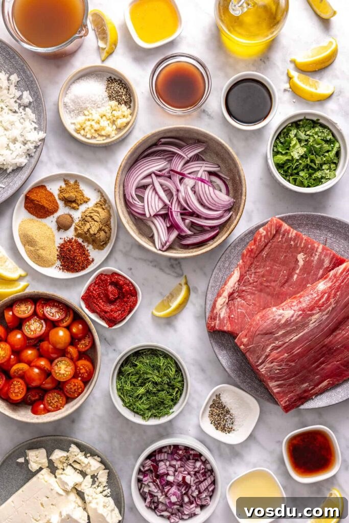 Overhead shot of ingredients for Greek beef bowls including flank steak, spices, tomatoes, herbs, and lemon