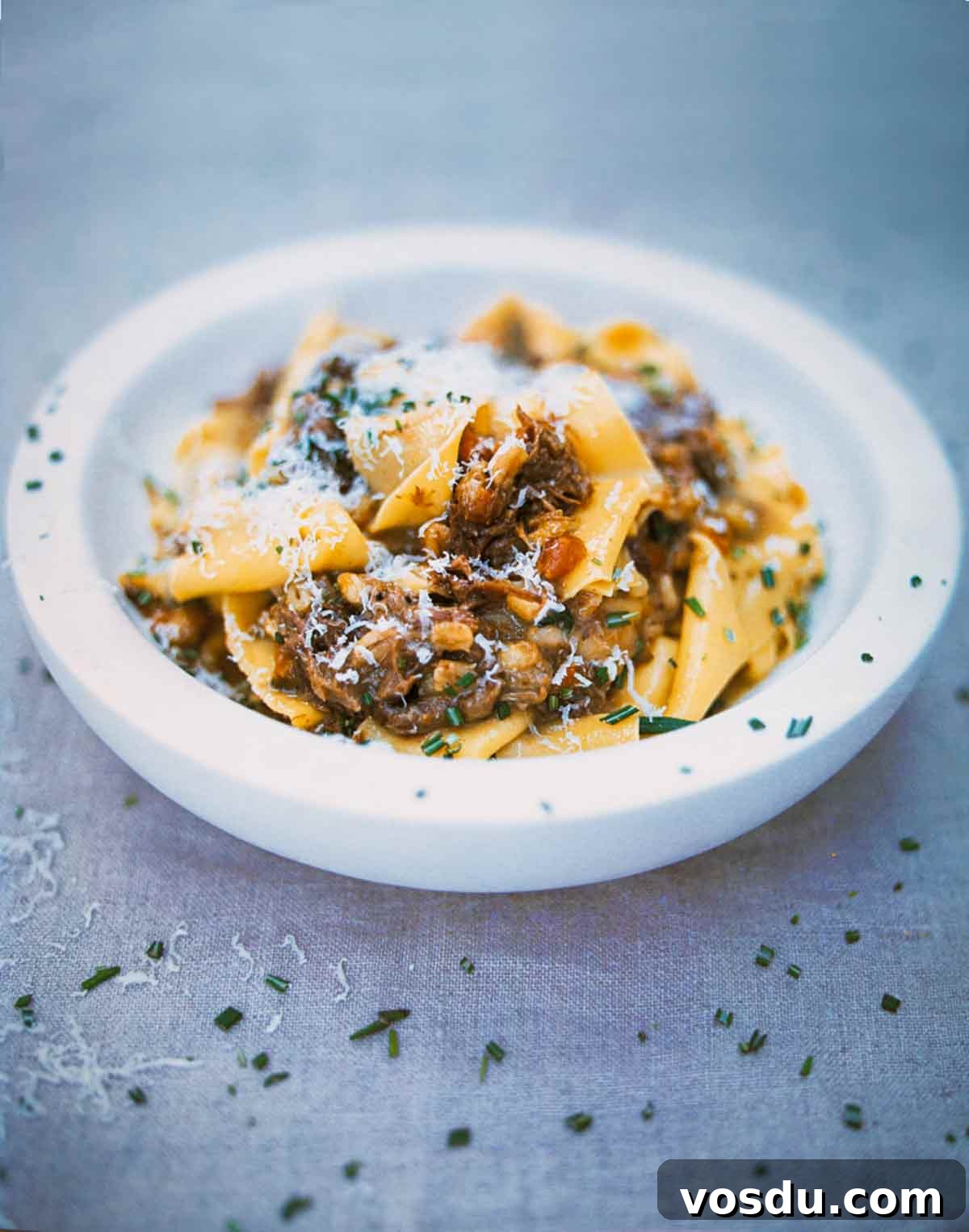Jamie Oliver Pappardelle with Beef Ragu Recipe 2 A white bowl filled with pappardelle pasta with Jamie Oliver's beef ragu sprinkled with chopped rosemary.